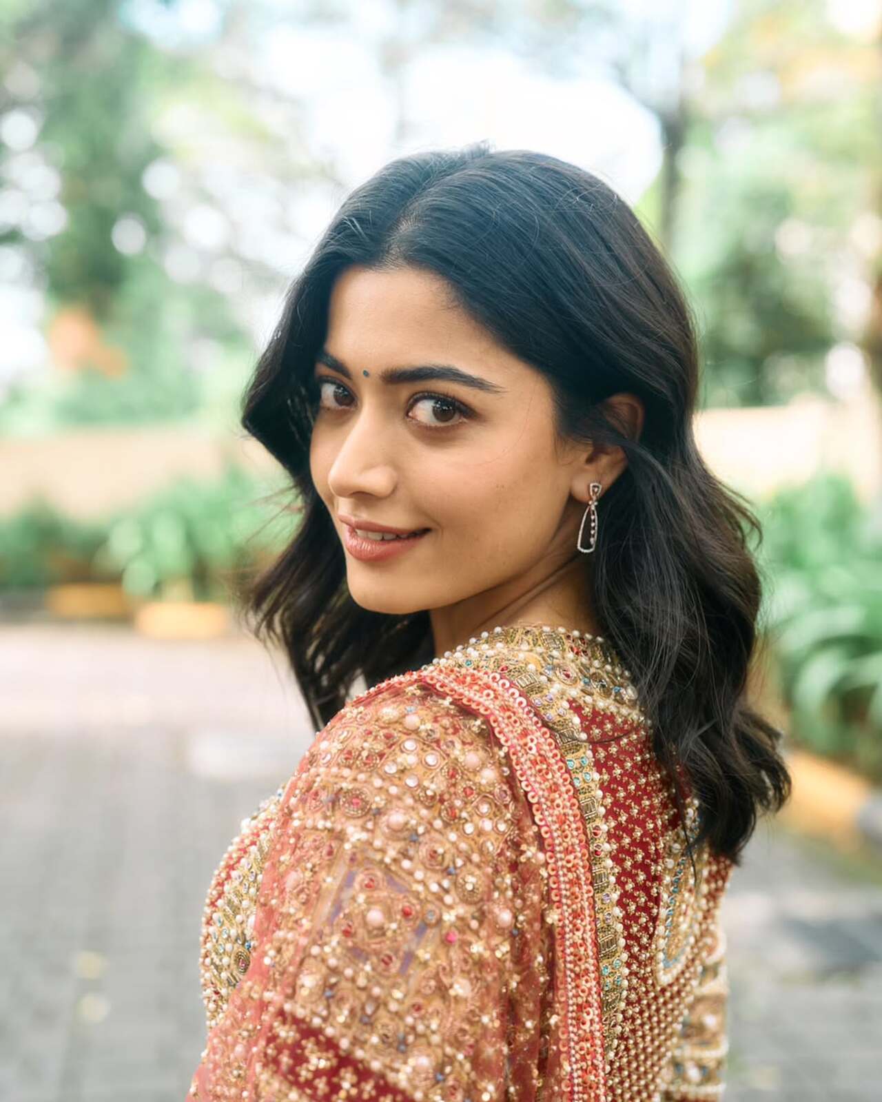 Rashmika Mandanna exudes festive radiance in this intricately embroidered red kurta set, making it a stellar choice for Ganesh Chaturthi. The deep maroon base adorned with detailed golden and pastel threadwork brings together tradition and artistry, while the sheer dupatta with delicate polka-dot detailing adds a touch of lightness